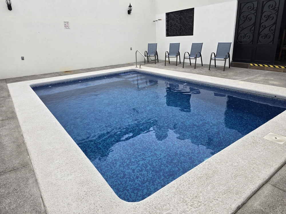 Alberca azul privada de Casa Atlántika, con patio y sillas al fondo.